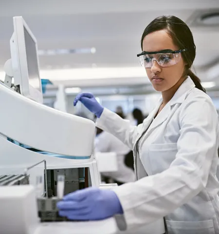 a young scientist wearing a white lab coat and protective eyewear works on equipment in a lab