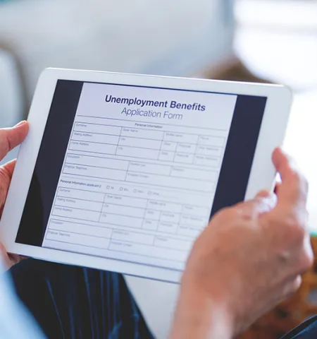 hands holding a computer tablet with an unemployment benefits application form open on it