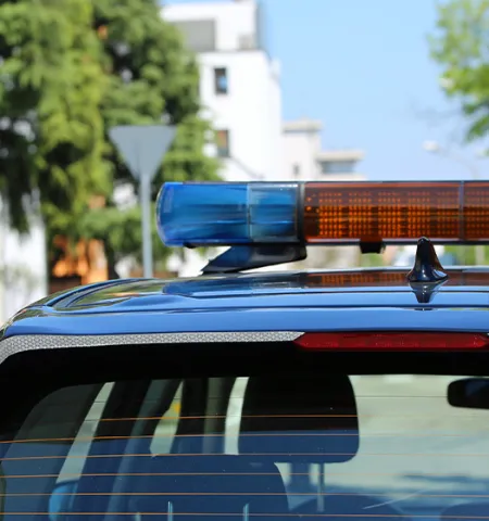 A police car with a blue and orange light bar on top, parked on a street with trees and buildings in the background (Credit: AdobeStock).