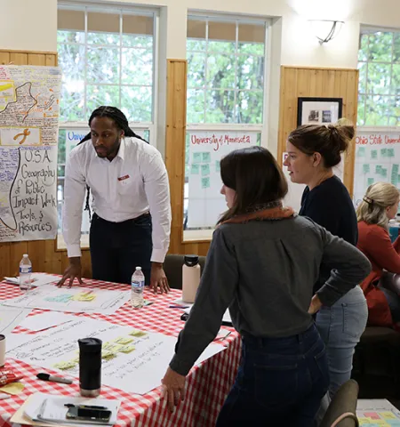 John Glenn College of Public Affairs Assistant Professor Victor St. John, second from left, stands around a table with (from left) Glenn College Professors Jill Clark and Stephanie Moulton looking at notes for discussion.