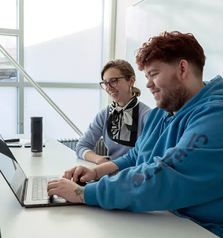 a professor and a student have a discussion in front of a computer in a brightly lit room