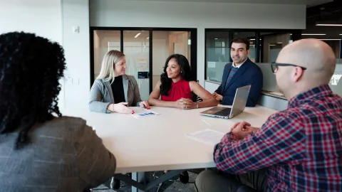 group of five adult professionals sitting around a table collaborating