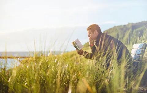 a person sitting on a bench outside reading a book 
