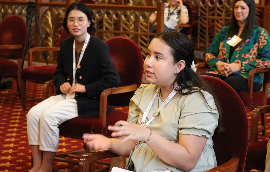 a student sitting in a chair speaking to a room. 