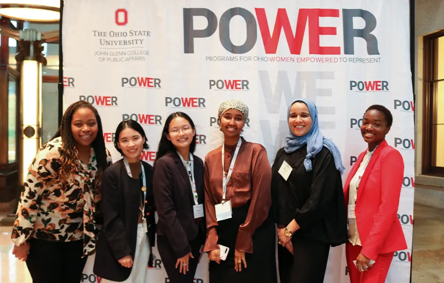 a group of women standing in front of a sign that reads POWER.