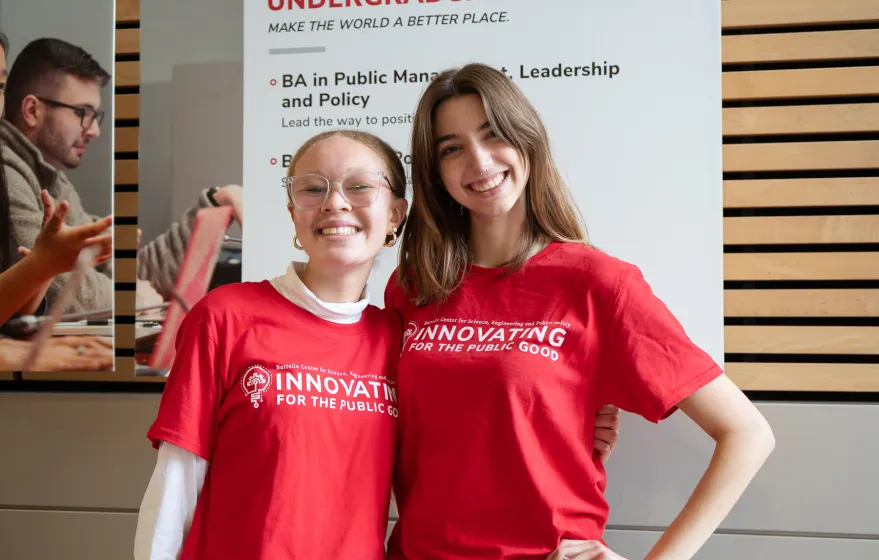 Two girls pose in red shirts. They are smiling.